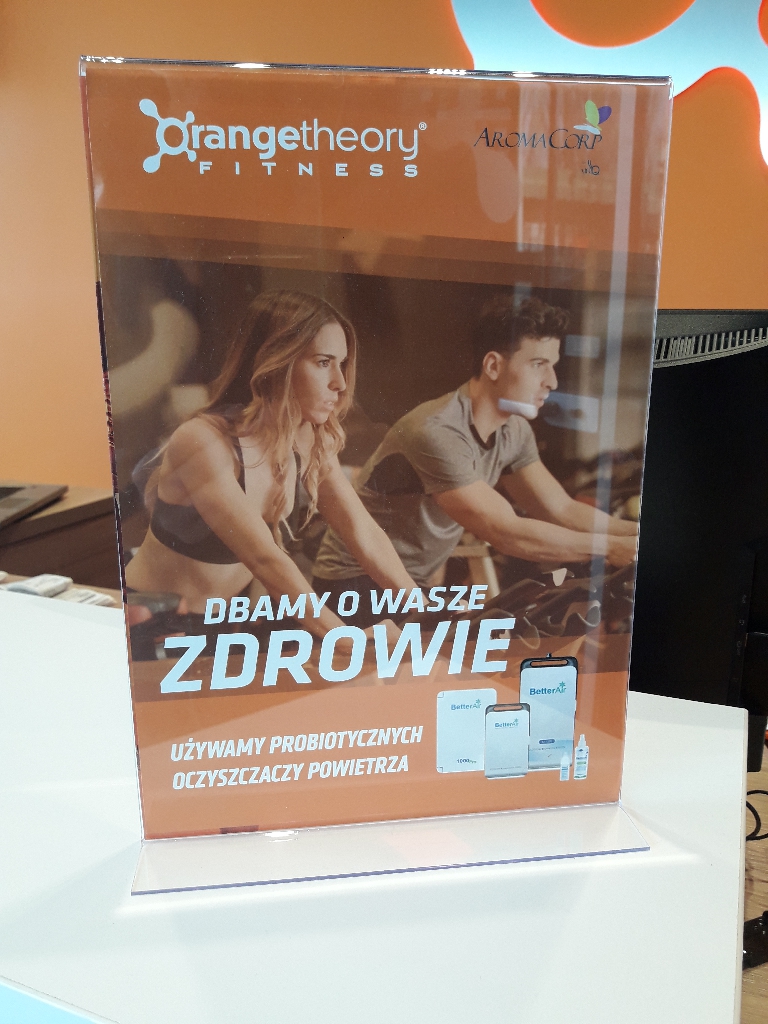 Akrylowy stojak informacyjny A4 z kolorowym plakatem w recepcji klubu fitness – przykład mobilnej ekspozycji.