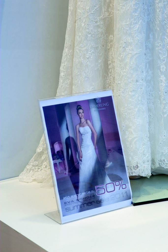Przezroczysty stojak akrylowy z plakatem promocyjnym ustawiony na wystawie salonu sukien ślubnych.