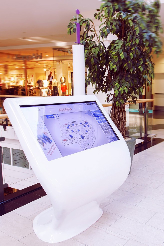 Interaktywny kiosk informacyjny w galerii handlowej Arkadia, wyświetlający mapę obiektu. Nowoczesne urządzenie ułatwiające nawigację i wyszukiwanie sklepów.