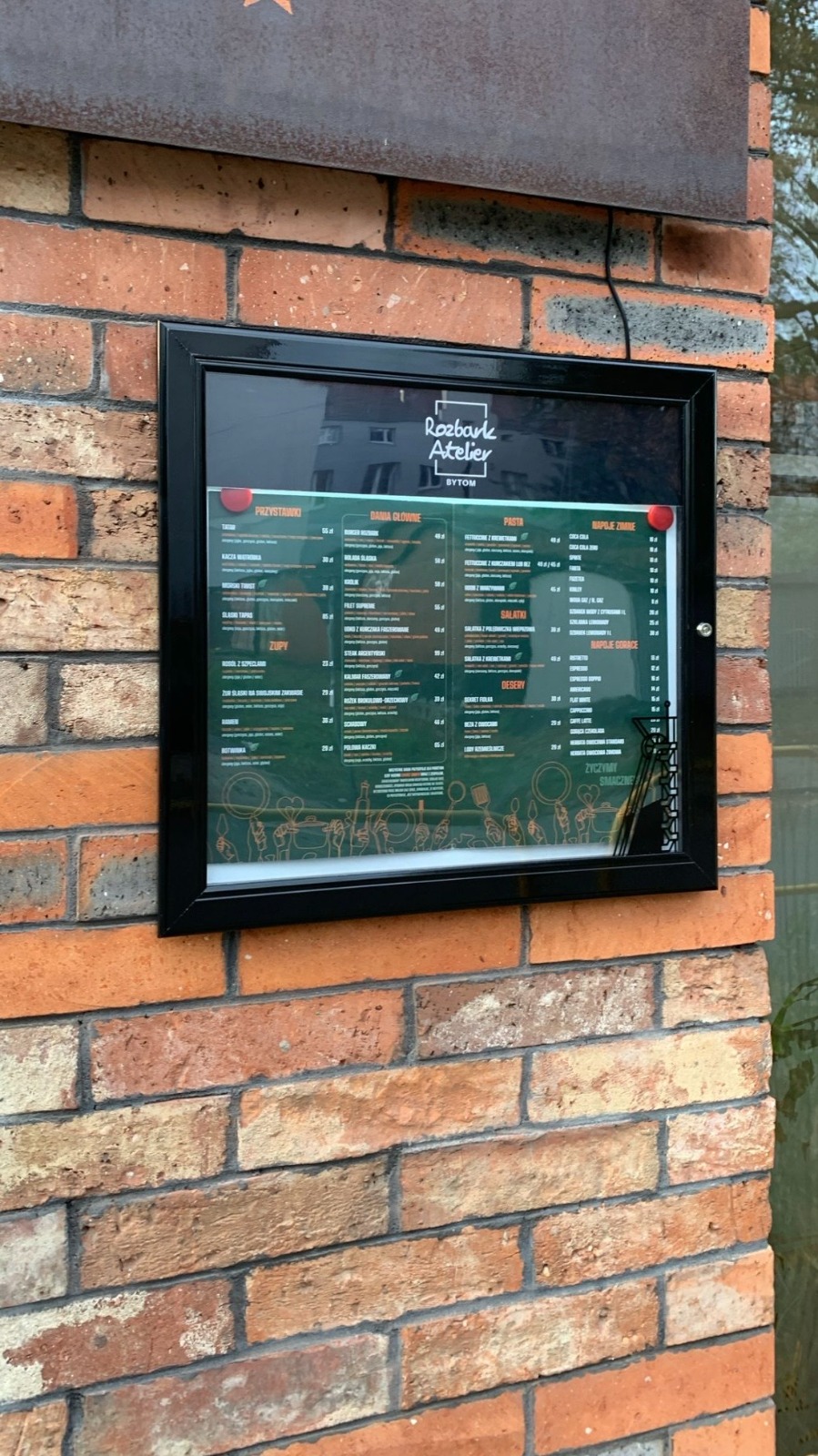 Gablota z menu restauracji Rozbark Atelier zamontowana na ceglanej ścianie lokalu.