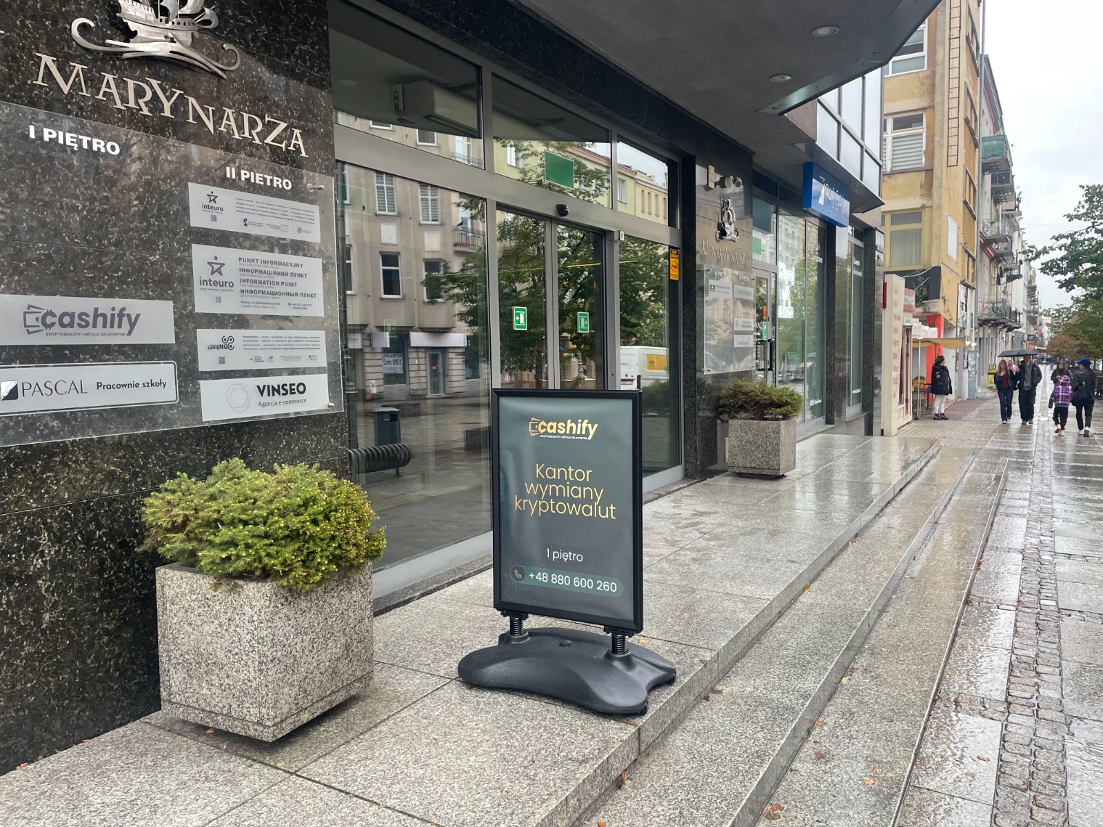 Potykacz reklamowy przed wejściem do kantoru kryptowalut Cashify w centrum miasta.