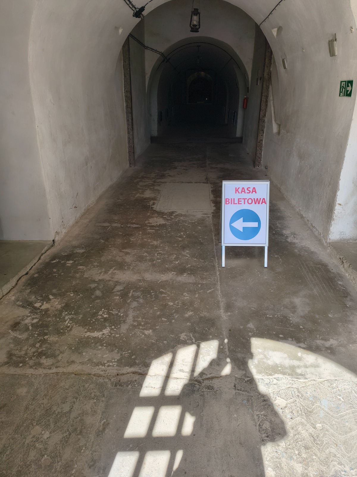 Potykacz informacyjny z napisem „Kasa biletowa” w korytarzu zabytkowego obiektu.