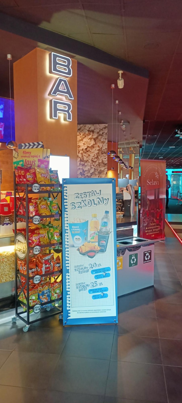 Roll-up promocyjny z ofertą zestawu szkolnego ustawiony przy barze kinowym.