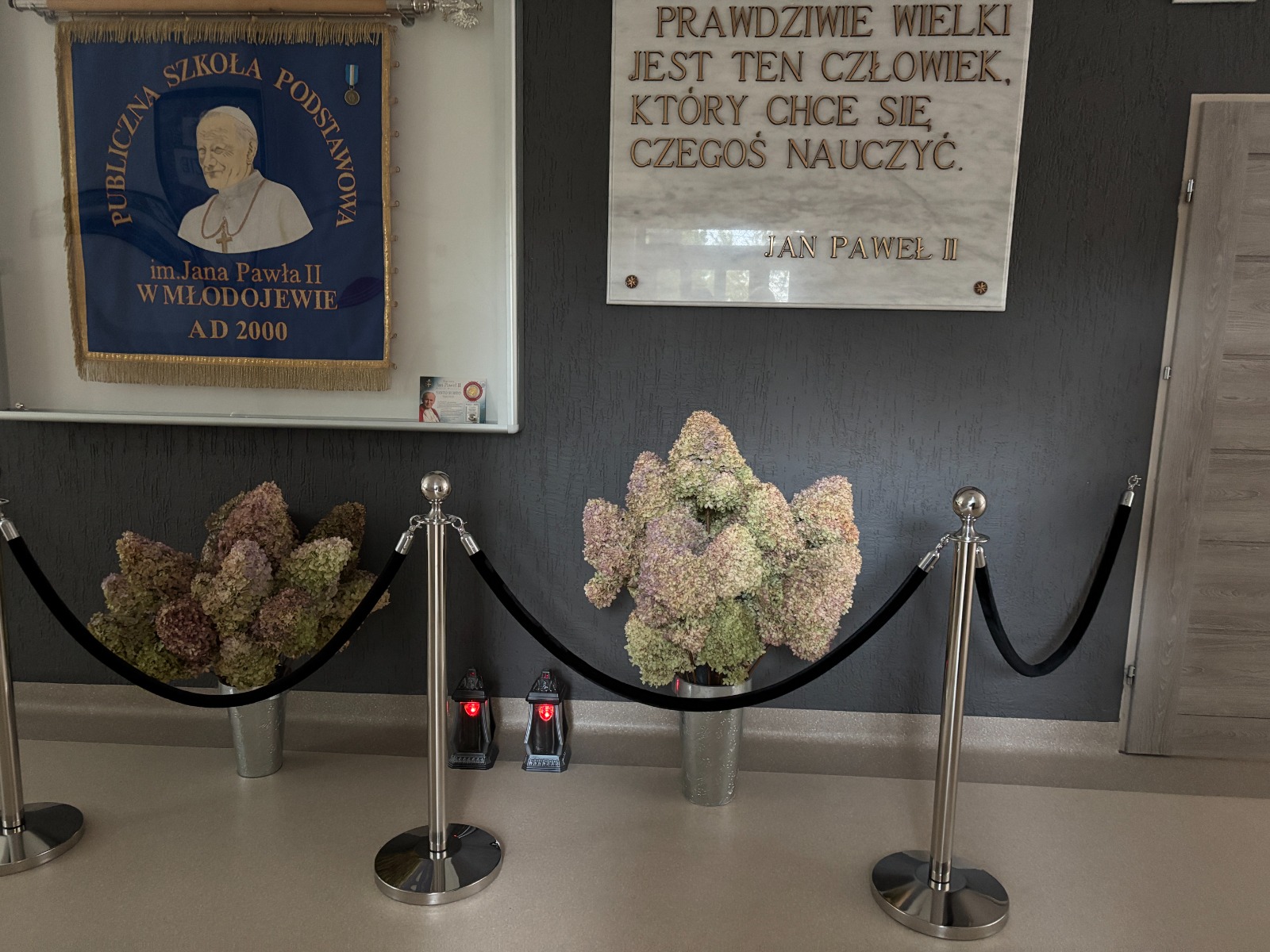 Chromowane słupki odgradzające z czarną liną w holu szkoły podstawowej.