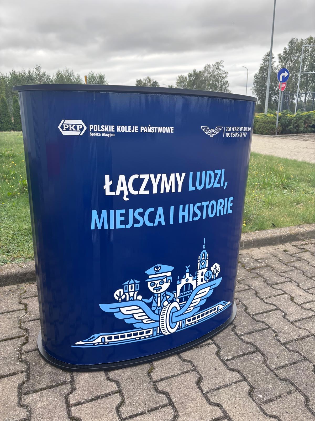 Trybunka promocyjna PKP z nadrukiem „Łączymy ludzi, miejsca i historie” w przestrzeni zewnętrznej.