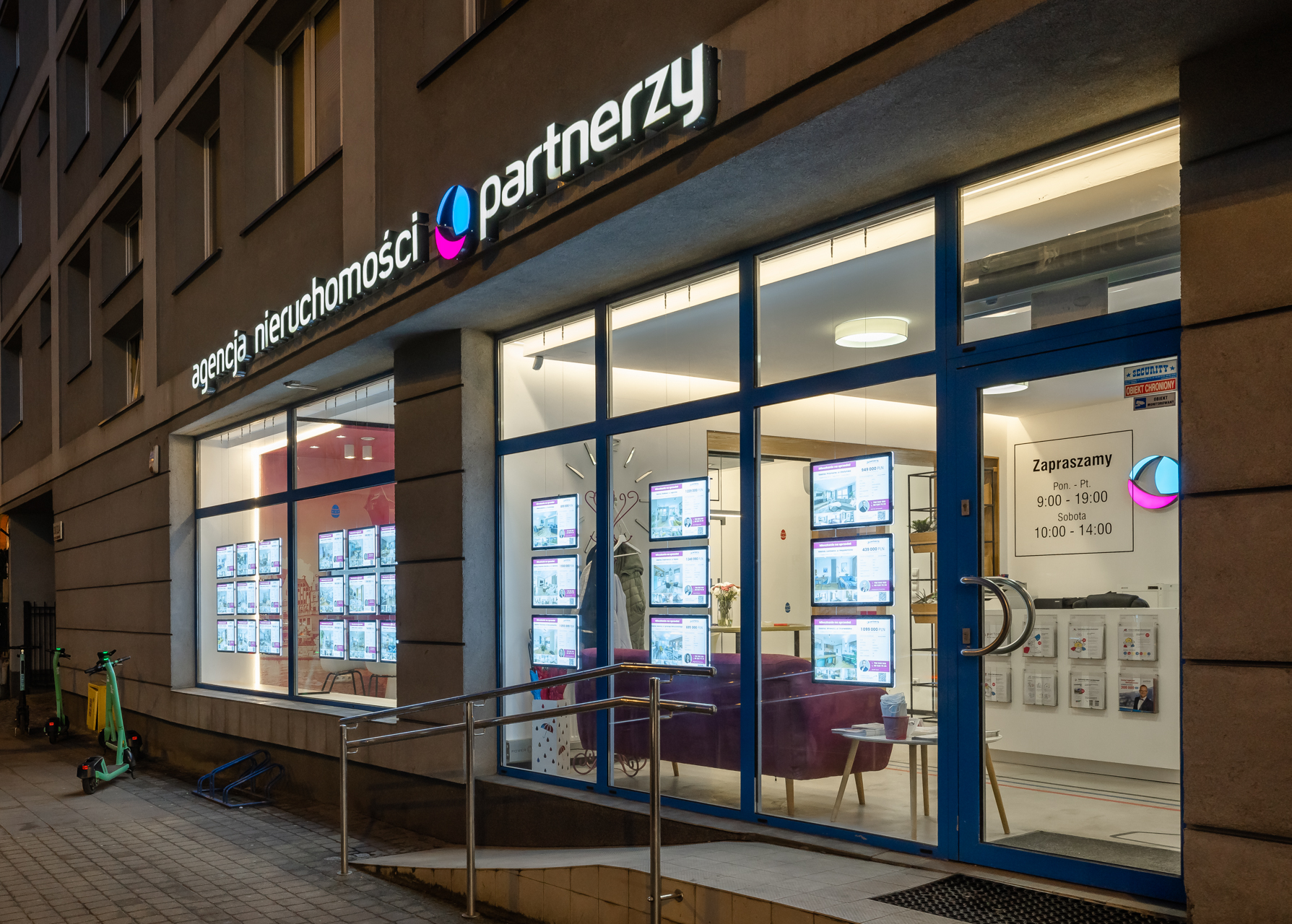 Podświetlane ramki LED w witrynie agencji nieruchomości, widoczne po zmroku