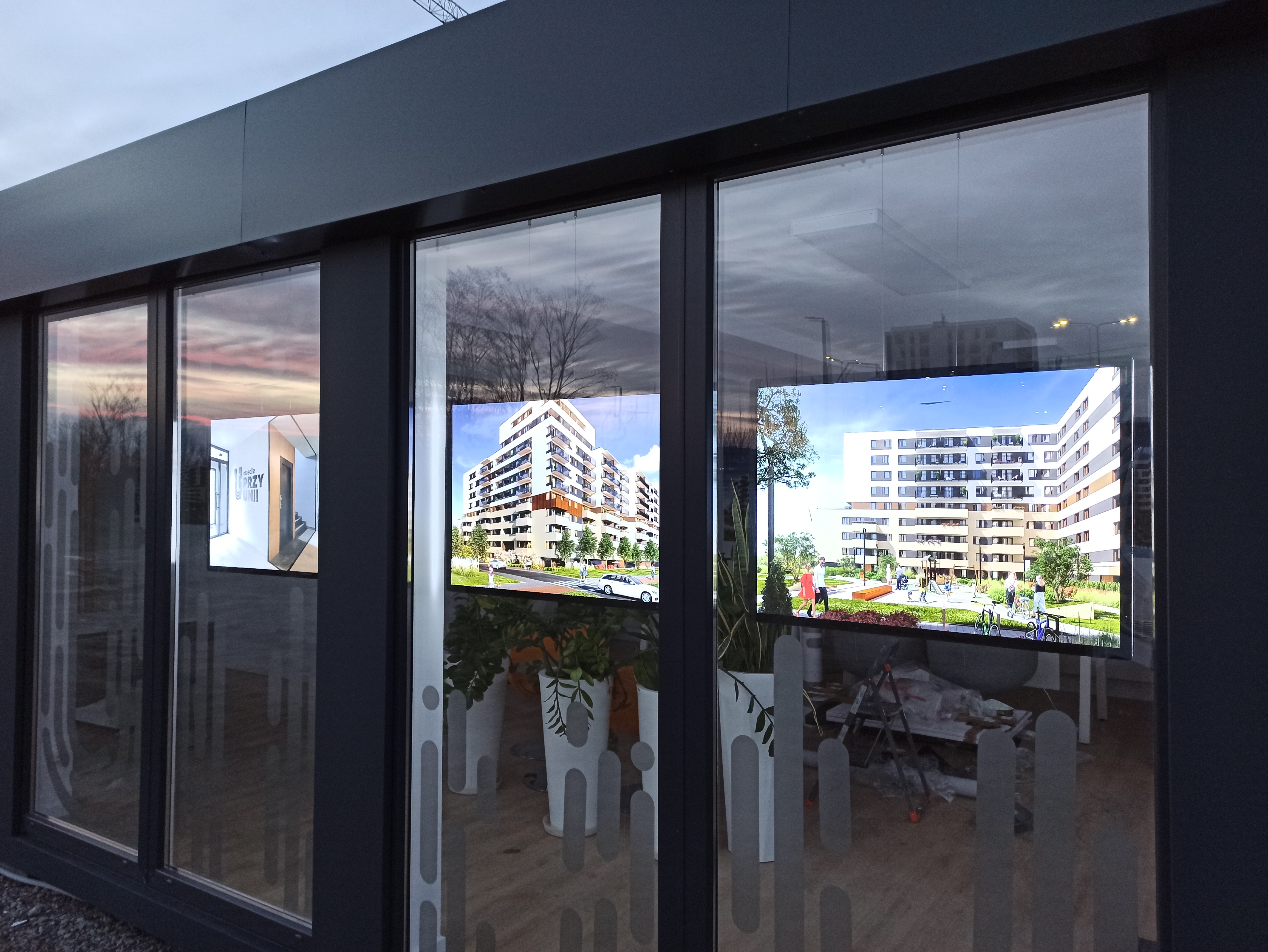 Monitory reklamowe w witrynie biura sprzedaży prezentujące wizualizacje inwestycji