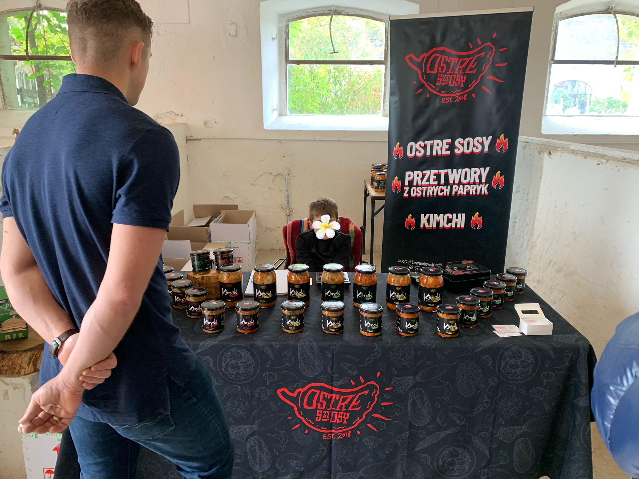 Stoisko z ostrymi sosami i czarnym roll-upem reklamowym z czerwonym napisem, promującym produkty lokalnej marki na targach