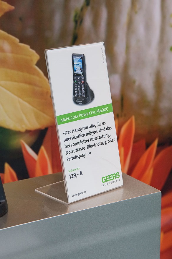 Akrylowy stojak informacyjny z ulotką prezentującą telefon komórkowy – ekspozycja w sklepie z elektroniką.