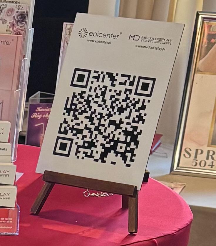 Wydruk z kodem QR ustawiony na sztaludze podczas targów – przykład połączenia druku z technologią.